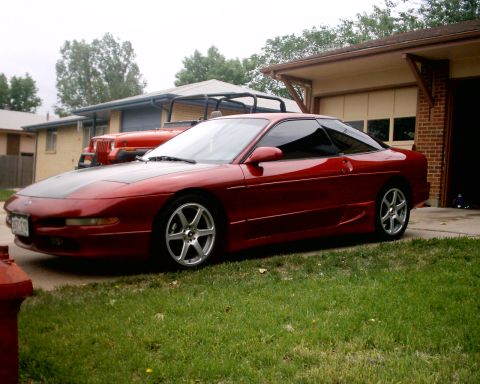 1994 Ford Probe - A red 1994 Ford Probe coupe is parked in front of a garage, with a Jeep visible behind it.