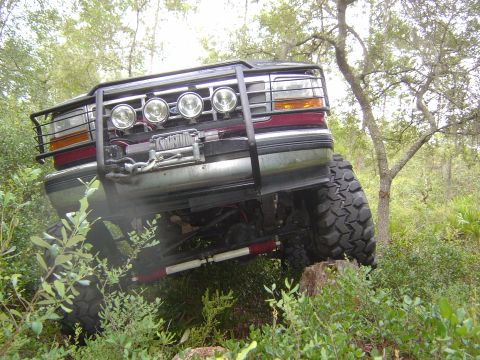1993 Ford Bronco - Modified 1993 Ford Bronco navigates a wooded trail with large off-road tires.