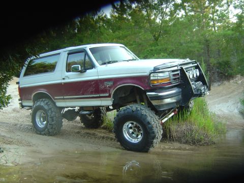 1993 Ford Bronco - Modified Ford Bronco with off-road tires and a custom front bumper navigates a muddy trail.