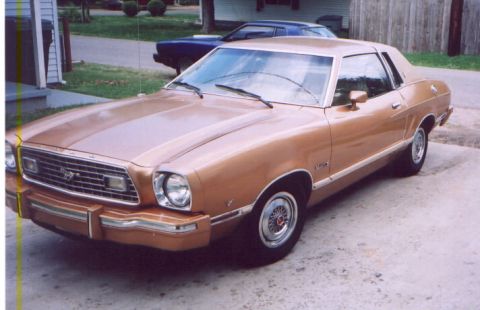 1978 Ford Mustang II - Tan 1978 Ford Mustang II coupe with chrome trim and wire wheels, parked outside.