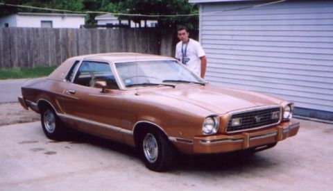 1978 Ford Mustang II - A bronze 1975 Ford Mustang II coupe is parked in front of a garage with a man standing beside it.