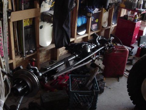 1987 Ford Bronco - A disassembled front axle assembly is shown in a garage setting, with snowboards on a shelf in the background.