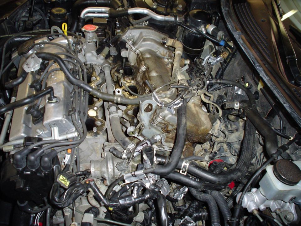 Engine bay with V6 engine partially disassembled, exposed intake area, hoses and wiring visible