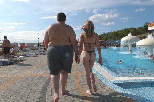 man and woman walking hand-in-hand on a paved path next to a swimming pool