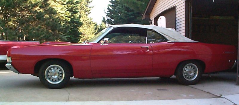 Red convertible with light-colored soft top, side view in driveway by a garage