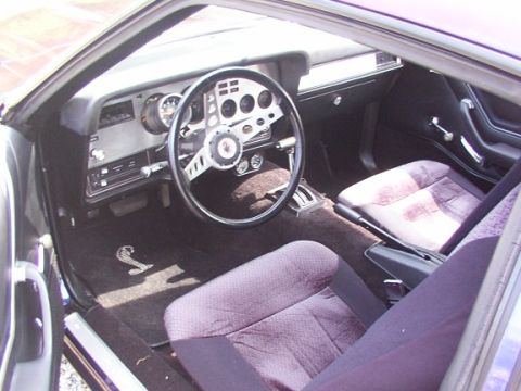 1978 Ford Mustang II - The interior of a 1978 Ford Mustang II Cobra II features a distinctive steering wheel and a Cobra snake emblem on the floor mat.