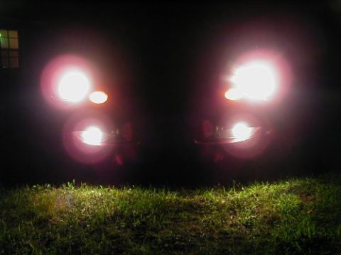1997 Ford Taurus - Headlights of a car are illuminated at night, casting light on the grass in front.