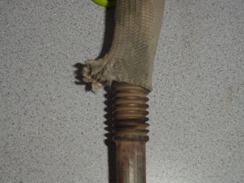 1987 Ford Bronco - Close-up of an exhaust pipe a frayed heat shield and a ribbed section, with a Supermotors.net watermark.