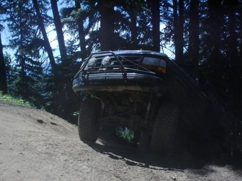 1995 Ford Bronco - This modified SUV is navigating a steep, dusty trail surrounded by dense forest.