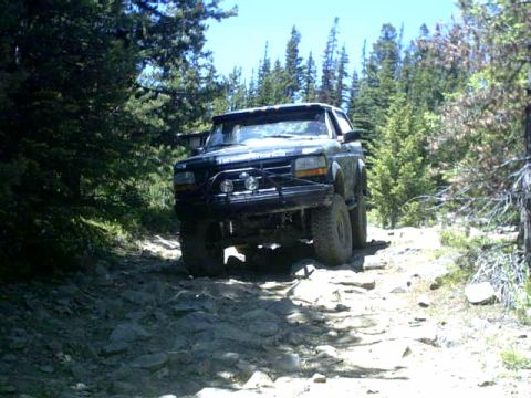 1995 Ford Bronco - A black Ford Bronco navigates a rough, rocky path through a forest.