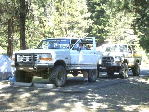 1995 Ford Bronco - Two trucks are parked on a dirt road, with a tent visible to the left.