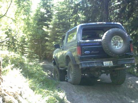 1995 Ford Bronco - A black Ford Bronco navigates a rocky, wooded trail with a spare tire on the rear.