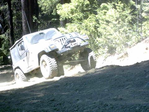 1995 Ford Bronco - White Jeep Wrangler TJ navigates a steep, dusty incline surrounded by trees.