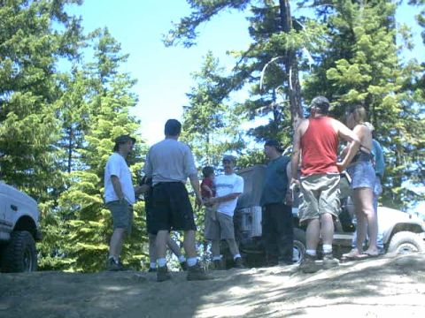 1995 Ford Bronco - Several people stand near SUVs and trucks in a wooded area, possibly at an off-road event.