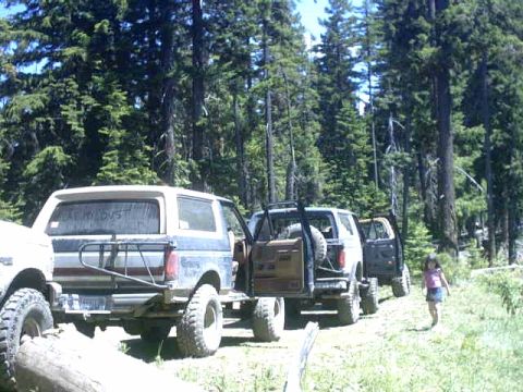 1995 Ford Bronco - A group of Ford Broncos are parked in a wooded area, with a young girl walking nearby.