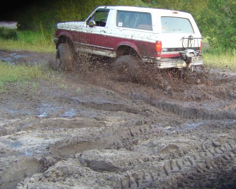 1993 Ford Bronco - This 1993 Ford Bronco is navigating a muddy trail, with tires spraying dirt and water.