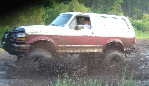 1993 Ford Bronco - Ford Bronco navigates a muddy off-road trail, kicking up a large spray.