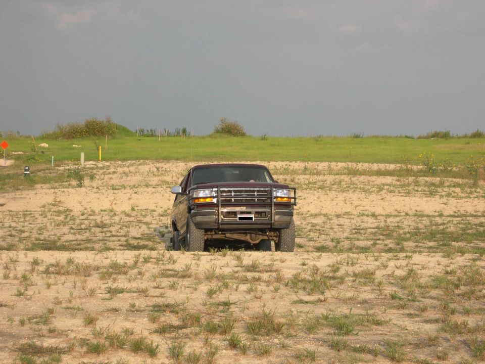 Lifted dark maroon Ford Bronco with grille guard facing camera on sandy off-road terrain