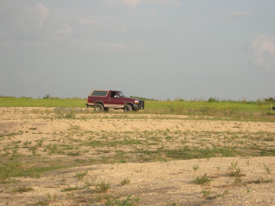 Distant dark vehicle on a barren dirt field, very low-resolution image