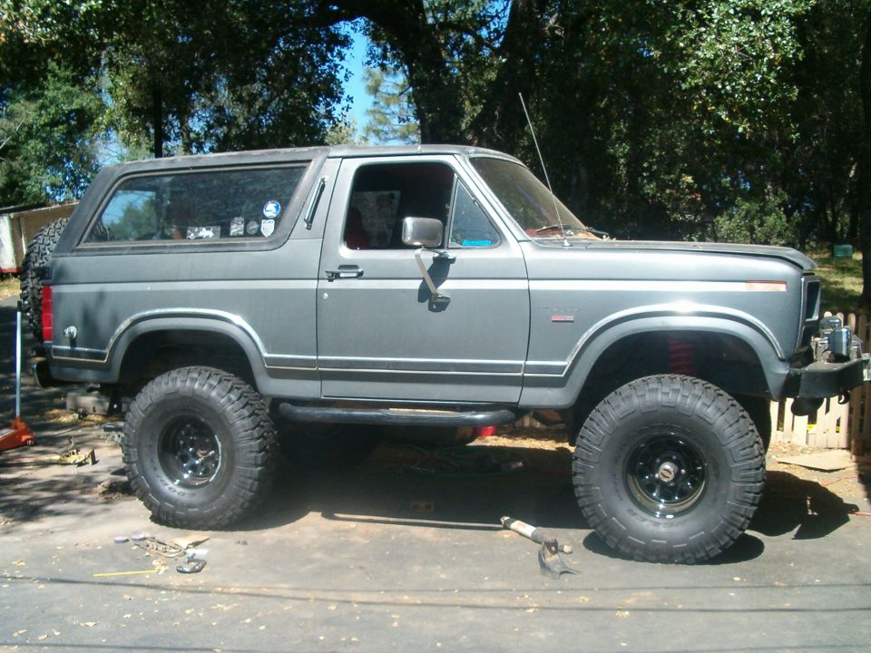 Gray lifted two-door Ford Bronco with large off-road tires, side view in a driveway with tools on the ground