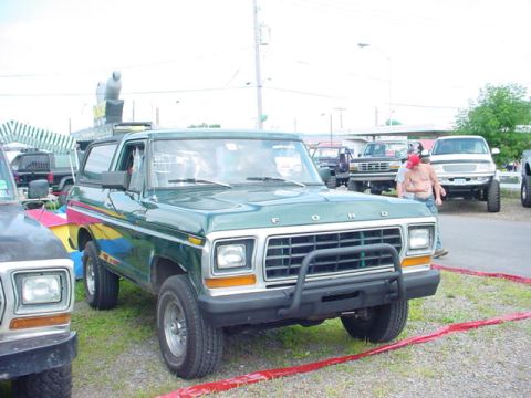 1979 Ford Bronco - A green Ford Bronco is parked outdoors with other vehicles and tents in the background.