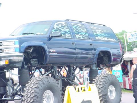 1979 Ford Bronco - A lifted blue monster truck with flame decals sits elevated on enormous tires.