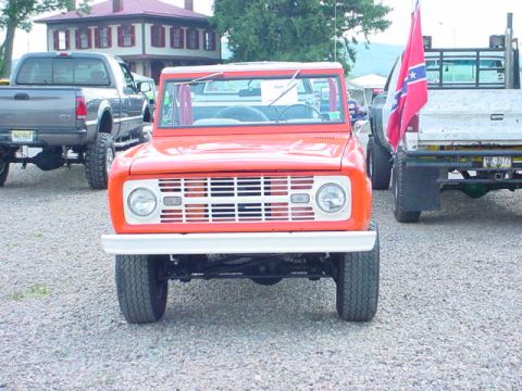 1979 Ford Bronco - An orange SUV is parked on a gravel lot next to a pickup truck.
