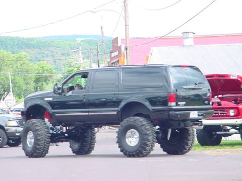 1979 Ford Bronco - Modified black SUV with massive tires, parked alongside a red truck.