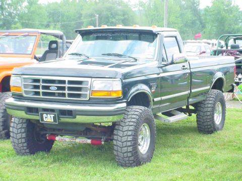 1979 Ford Bronco - Lifted black Ford F-Series pickup truck with oversized tires parked on grass.