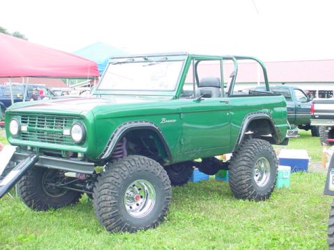 1979 Ford Bronco - A modified green Ford Bronco sits on a grassy field, with other vehicles and tents in the background.
