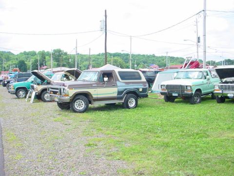 1979 Ford Bronco - A line of SUVs and trucks are parked on a grassy field, with the brown and tan Bronco in the foreground.