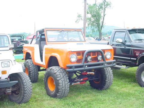 1979 Ford Bronco - An orange 1978 Ford Bronco is parked next to other vehicles, modified with off-road tires and lights.