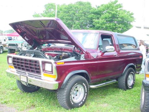 1979 Ford Bronco - This maroon Ford Bronco has its hood open, revealing the engine bay. It is parked outdoors on a grassy area.