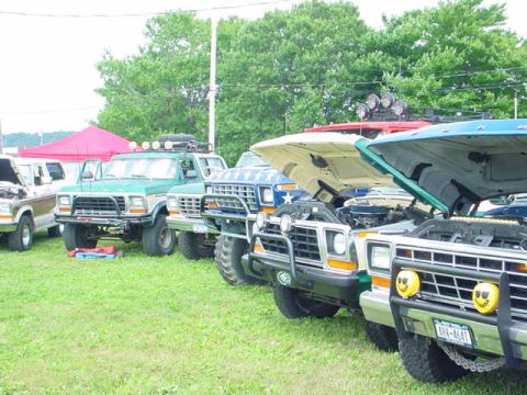 1979 Ford Bronco - Multiple 1979 Ford Broncos and trucks are lined up on a grassy field with their hoods open.