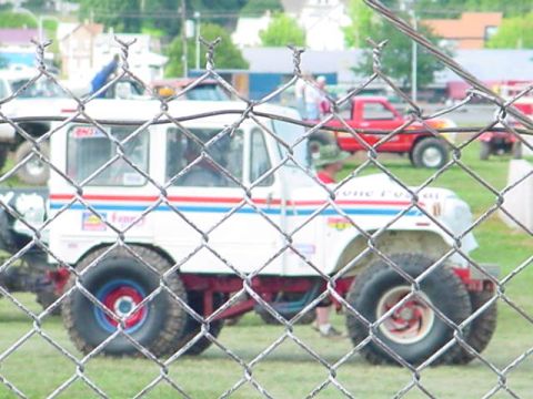 1979 Ford Bronco - A customized off-road vehicle with prominent tires is seen behind a chain-link fence, with other vehicles in the background.