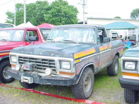 1979 Ford Bronco - A weathered 1979 Ford Bronco sits parked on grass next to another vehicle, with tents in the background.