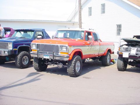 1979 Ford Bronco - This lifted pickup truck features a two-tone orange and tan paint scheme and a prominent chrome grille. The license plate is visible.