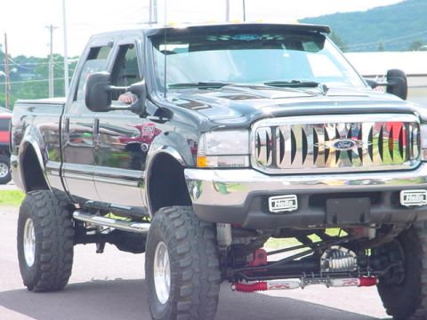 1979 Ford Bronco - A heavily modified black Ford pickup truck is shown with a prominent chrome grille and oversized off-road tires.