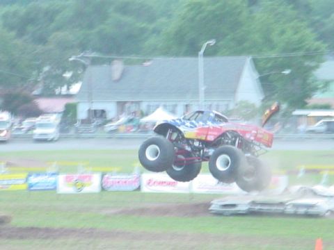 1979 Ford Bronco - A monster truck soars through the air, crushing cars below during an event.
