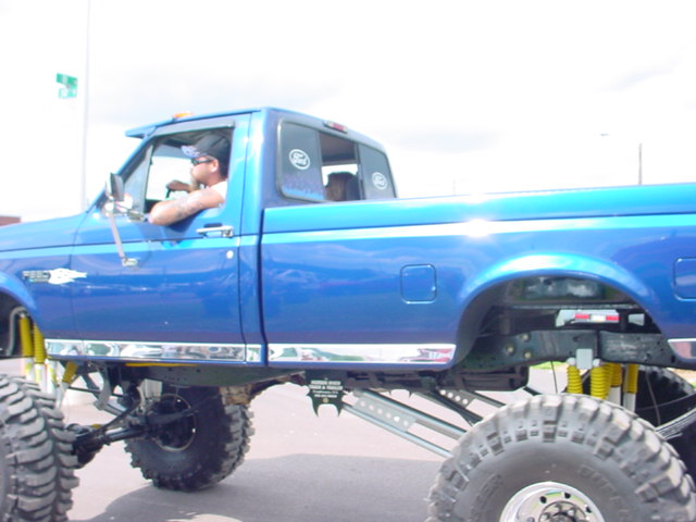 Side view of a lifted blue pickup truck with large tires and yellow suspension