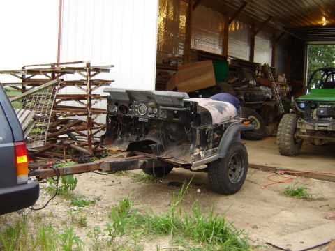 1992 Ford Bronco - A disassembled Jeep CJ-7 chassis is towed on a trailer inside a barn, with a green Suzuki Samurai visible in the background.