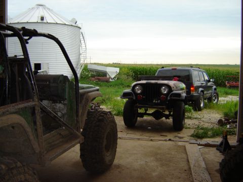1992 Ford Bronco - Two off-road vehicles and a dark SUV are parked in front of a farm silo.