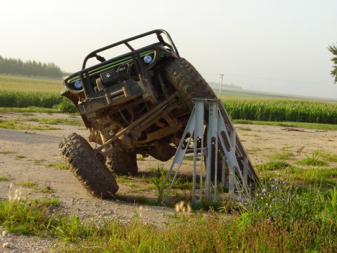 1992 Ford Bronco - An off-road vehicle is stuck on a metal ramp in a field with corn in the background.