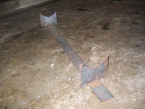 1978 Ford Bronco - Shop-built steel fabrication jig sitting on a stained concrete floor: a long flat bar with a V-notched vertical cradle plate welded at each…