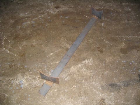1978 Ford Bronco - Shop-fabricated steel crossmember or alignment jig lying on a dirty concrete garage floor, made from a long flat bar with angled steel plat…