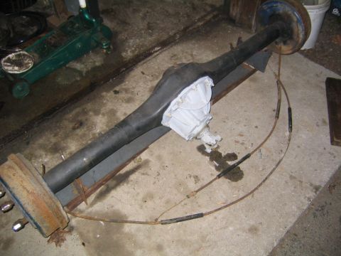 1978 Ford Bronco - A complete rear axle assembly removed from a vehicle and laid on a garage floor, with dark axle tubes, a freshly white-painted differential…