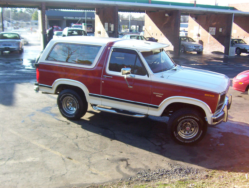 1986 Ford Bronco parked outside a car wash, red and white two-tone paint, white removable top