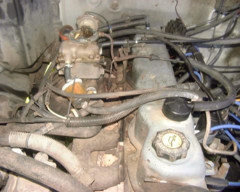 1985 Ford F-150 - Close-up of an engine bay, focusing on the carburetor and a fluid reservoir.