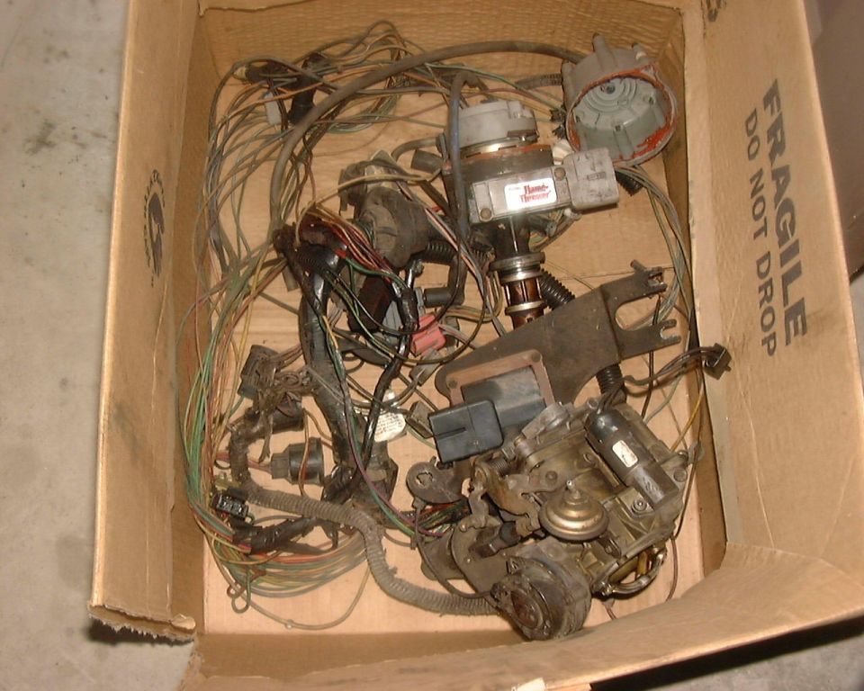 Cardboard box on a concrete floor full of pulled distributor, coil, carburetor and engine wiring