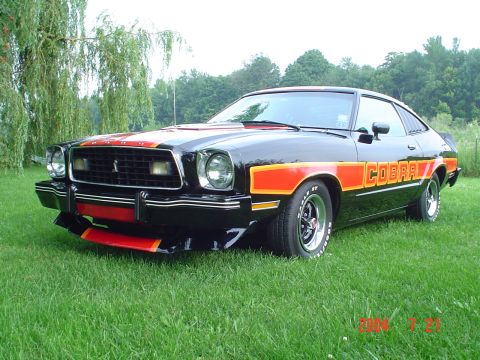 1978 Ford Mustang II - A black 1976 Ford Mustang II Cobra with distinctive orange and red racing stripes is shown from a three-quarter front view.